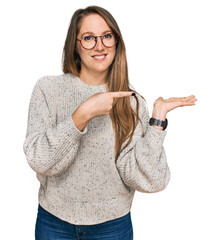 Canvas Print - Young blonde woman wearing casual sweater and glasses amazed and smiling to the camera while presenting with hand and pointing with finger.