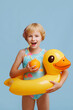 © Kaplitskaya Love - A child in a blue-orange swimsuit with an inflatable duck ring on a blue background. Drinks orange juice with a straw. The concept of a fun summer holiday on the beach or pool.