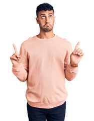 Poster - Young hispanic man wearing casual clothes pointing up looking sad and upset, indicating direction with fingers, unhappy and depressed.