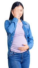 Sticker - Young beautiful chinese woman pregnant expecting baby covering one eye with hand, confident smile on face and surprise emotion.