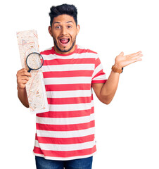 Sticker - Handsome latin american young man looking at city map with magnifying glass celebrating victory with happy smile and winner expression with raised hands