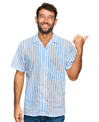 Sticker - Handsome young man with beard wearing casual fresh shirt smiling with happy face looking and pointing to the side with thumb up.