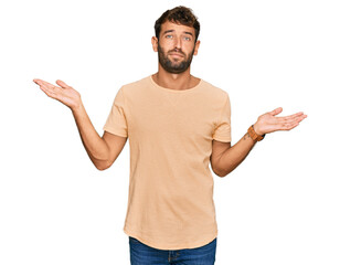 Canvas Print - Handsome young man with beard wearing casual tshirt clueless and confused expression with arms and hands raised. doubt concept.