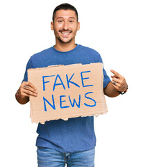 Poster - Handsome man with tattoos holding fake news banner smiling happy pointing with hand and finger