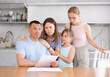 Thoughtful man reads expense estimate document and is saddened by bad news about financial situation, upset dad is supported and hugged by children and wife.