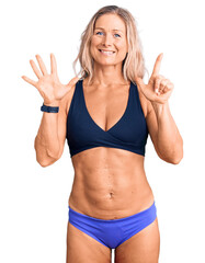 Wall Mural - Middle age fit blonde woman wearing bikini showing and pointing up with fingers number seven while smiling confident and happy.