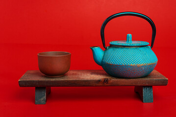 Wall Mural - cast iron asian teapot with clay cup on wooden stand on red background