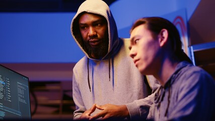 Poster - BIPOC hackers in dimly lit room discussing ways to breach defenses and exploit weaknesses in PC systems. Evil cybersecurity gurus in hidden base getting past companies security networks