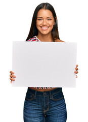 Canvas Print - Beautiful hispanic woman holding blank empty banner looking positive and happy standing and smiling with a confident smile showing teeth