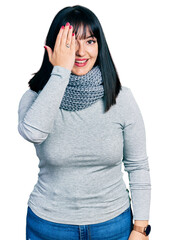 Poster - Young hispanic plus size woman wearing winter scarf covering one eye with hand, confident smile on face and surprise emotion.