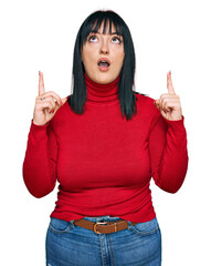 Canvas Print - Young hispanic woman wearing casual clothes amazed and surprised looking up and pointing with fingers and raised arms.