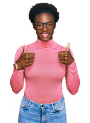 Poster - Young african american girl wearing casual clothes and glasses success sign doing positive gesture with hand, thumbs up smiling and happy. cheerful expression and winner gesture.