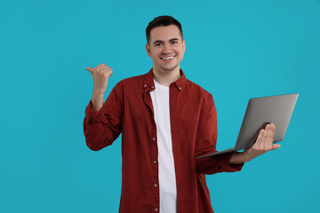 Special promotion. Happy young man with laptop pointing at something on light blue background, space for text