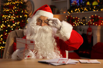 Wall Mural - Santa Claus holding letter at table in room decorated for Christmas