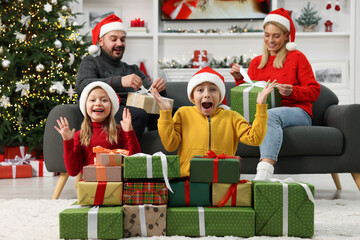 Poster - Parents and their surprised children in Santa hats with Christmas gifts at home