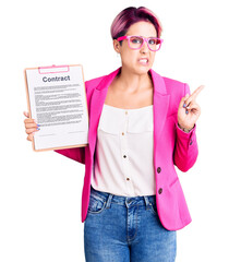 Canvas Print - Young beautiful woman with pink hair holding clipboard with contract document pointing aside worried and nervous with forefinger, concerned and surprised expression