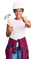 Poster - Young african american woman with braids wearing hardhat holding hammer annoyed and frustrated shouting with anger, yelling crazy with anger and hand raised