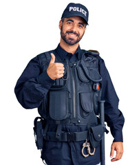 Wall Mural - Young hispanic man wearing police uniform doing happy thumbs up gesture with hand. approving expression looking at the camera showing success.