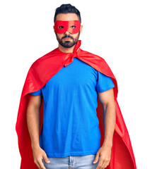 Poster - Young hispanic man wearing super hero costume with serious expression on face. simple and natural looking at the camera.