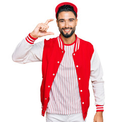 Canvas Print - Young man with beard wearing baseball uniform smiling and confident gesturing with hand doing small size sign with fingers looking and the camera. measure concept.