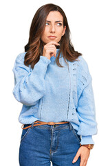 Wall Mural - Young brunette woman wearing casual winter sweater with hand on chin thinking about question, pensive expression. smiling with thoughtful face. doubt concept.