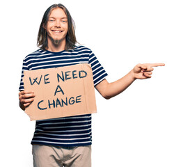 Sticker - Handsome caucasian man with long hair holding we need a change banner smiling happy pointing with hand and finger to the side