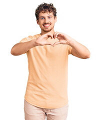 Wall Mural - Young handsome man with curly hair wearing casual clothes smiling in love showing heart symbol and shape with hands. romantic concept.