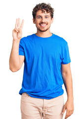 Wall Mural - Young handsome man with curly hair wearing casual clothes showing and pointing up with fingers number three while smiling confident and happy.