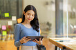 © Songsak C - A beautiful Asian businesswoman holding a digital tablet while standing in the office room. Business concept.