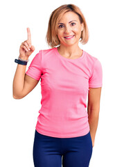 Poster - Young blonde woman wearing sportswear showing and pointing up with finger number one while smiling confident and happy.