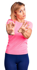 Poster - Young blonde woman wearing sportswear moving away hands palms showing refusal and denial with afraid and disgusting expression. stop and forbidden.