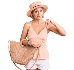 Sticker - Young blonde woman wearing summer hat holding bag with angry face, negative sign showing dislike with thumbs down, rejection concept