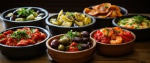 A Tempting Assortment Of Spanish Tapas, Featuring Patatas Bravas, Chorizo In Red Wine, Garlic Shrimp, Marinated Olives, And  Cheese, Artfully Presented On Small Plates And Wooden Boards.