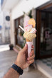 Man holding beautiful ice-cream italian gelato on sugar cone with multiple flavors, in front of ice cream store, Italy