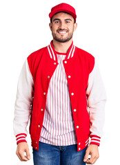 Wall Mural - Young handsome man wearing baseball jacket and cap looking positive and happy standing and smiling with a confident smile showing teeth