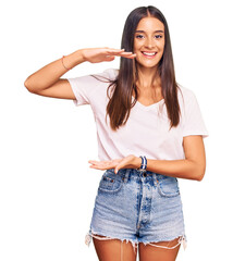 Wall Mural - Young hispanic woman wearing casual white tshirt gesturing with hands showing big and large size sign, measure symbol. smiling looking at the camera. measuring concept.