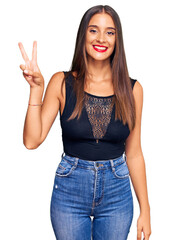 Wall Mural - Young hispanic woman wearing casual clothes showing and pointing up with fingers number two while smiling confident and happy.