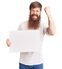 Canvas Print - Handsome young red head man with long beard holding blank empty banner annoyed and frustrated shouting with anger, yelling crazy with anger and hand raised