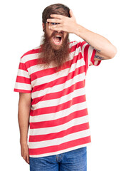 Poster - Handsome young red head man with long beard wearing casual clothes peeking in shock covering face and eyes with hand, looking through fingers with embarrassed expression.