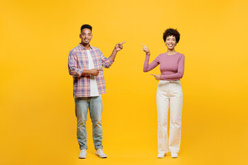 Poster - Full body young happy couple two friends family man woman of African American ethnicity wears casual clothes together point index finger aside on area between them isolated on plain yellow background.