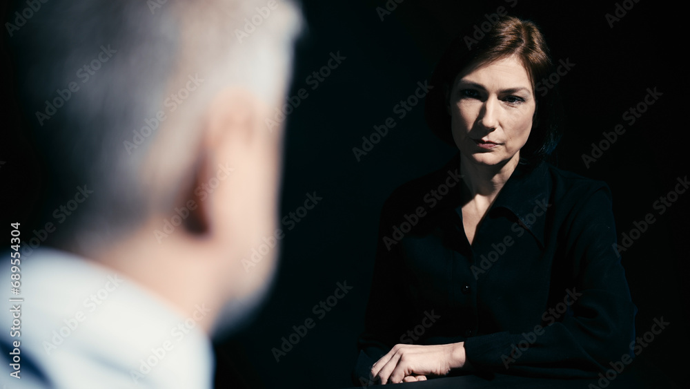 In a police interrogation scene, a detective is talking to and showing photos of the crime scene to a suspect