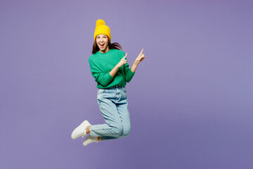 Sticker - Full body young woman she wear green sweater yellow hat casual clothes jump high point index finger aside on area isolated on plain pastel light purple background studio portrait. Lifestyle concept.