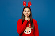 Merry young Latin woman wear red Christmas sweater fun decorative deer horns on head posing say hush be quiet with finger on lips shhh gesture isolated on plain blue background Happy New Year concept
