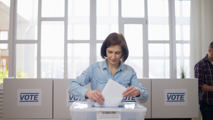 Wall Mural - A responsible middle-aged woman is voting at the polling station, throwing a ballot into the box