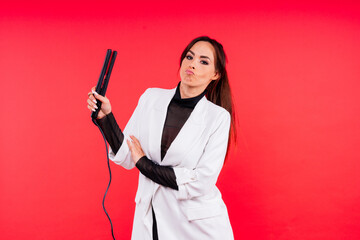 Happy young woman with beautiful hair holding curling iron on grey and red background