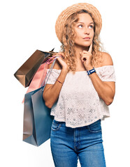 Wall Mural - Beautiful caucasian woman holding shopping bags serious face thinking about question with hand on chin, thoughtful about confusing idea