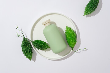 Sticker - Advertising photo for cosmetic of product with ingredient from bitter melon. A green bottle unlabeled on round ceramic dish with fresh bitter melons on a white background. Top view