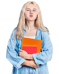 Sticker - Young caucasian woman holding books puffing cheeks with funny face. mouth inflated with air, catching air.