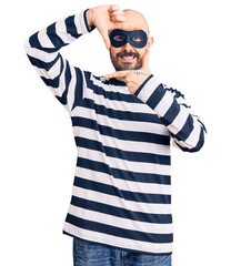 Poster - Young handsome man wearing burglar mask smiling making frame with hands and fingers with happy face. creativity and photography concept.