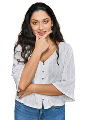 Wall Mural - Brunette young woman wearing casual clothes looking confident at the camera smiling with crossed arms and hand raised on chin. thinking positive.